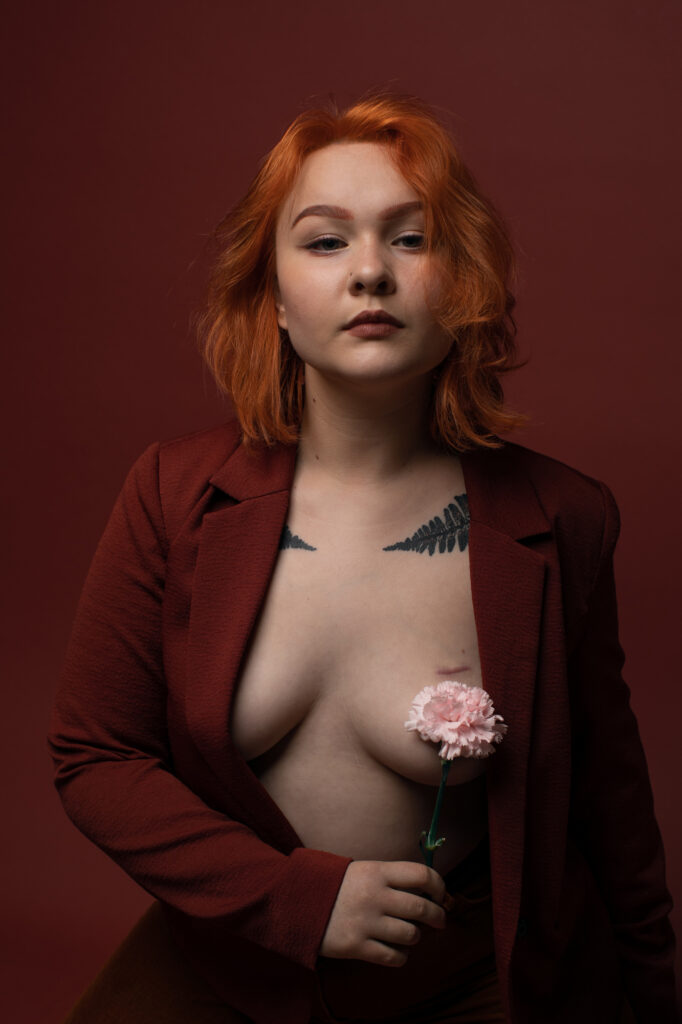 Zmysłowy portret rudowłosej kobiety w bordowej marynarce z różowym goździkiem - nastrojowa fotografia kobieca